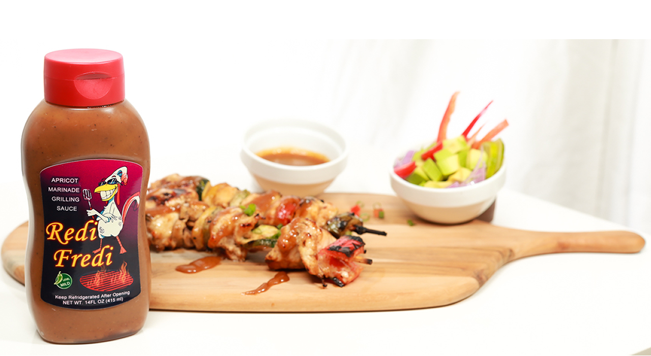 Redi Fredi bottle with a pair of grilled chicken and veggies shish kabob sticks on a wood board in the background.